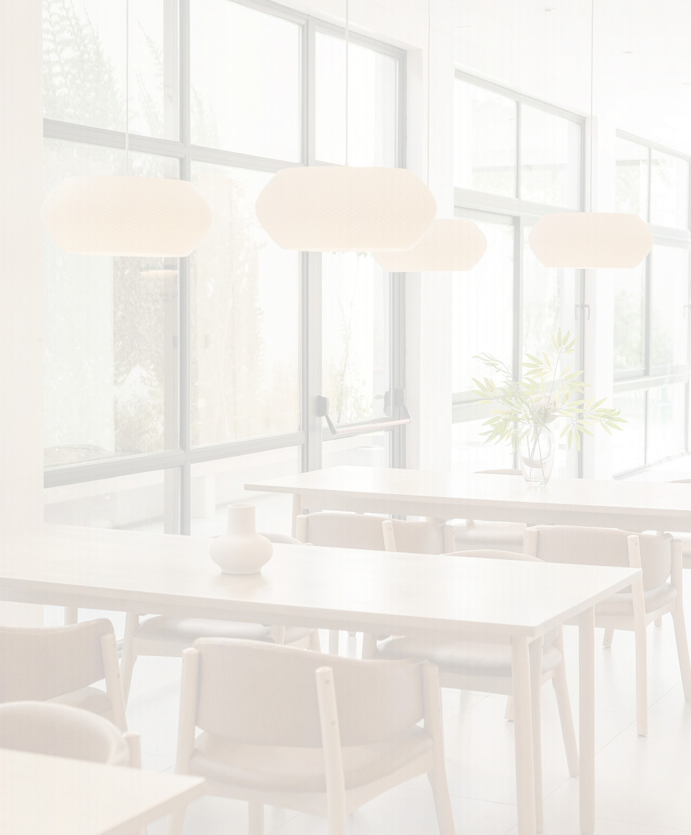 Interior luminoso con mesas de madera clara y lámparas suspendidas junto a grandes ventanales.